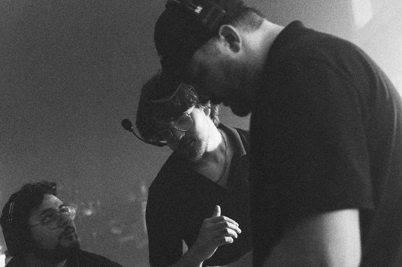 Behind the scenes on INERTIA: crew members in headsets huddle over a monitor in dim light.