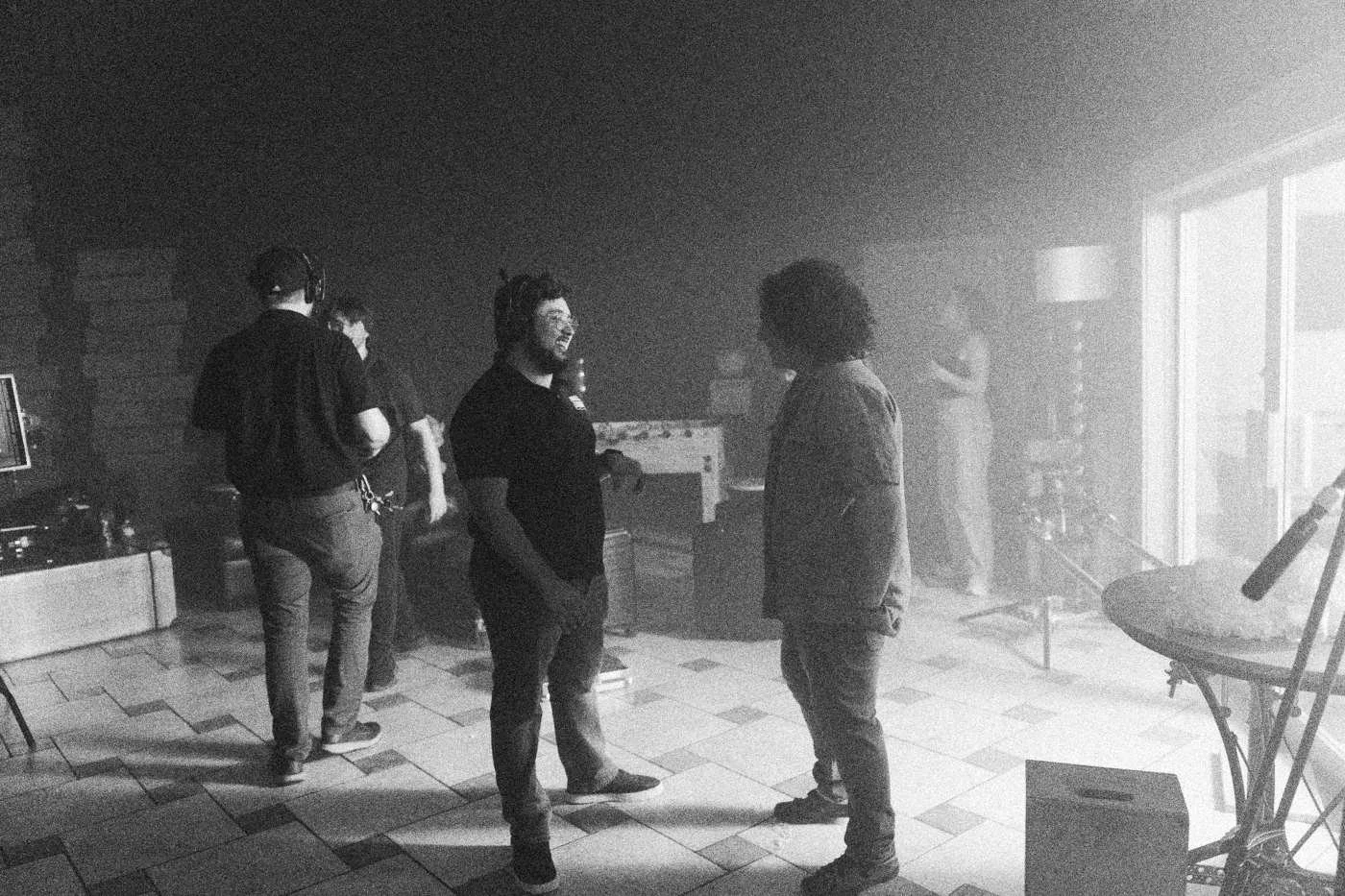 Behind the scenes on INERTIA: crew members stand talking in a pale hazy room with a patterned floor.