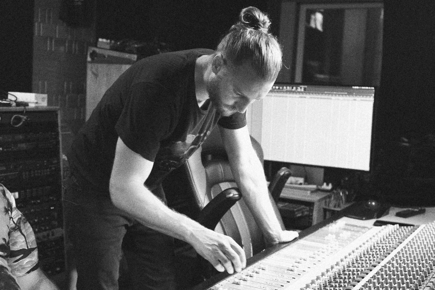 Behind the scenes on INERTIA: a man with his hair tied up leans over a mixing console.