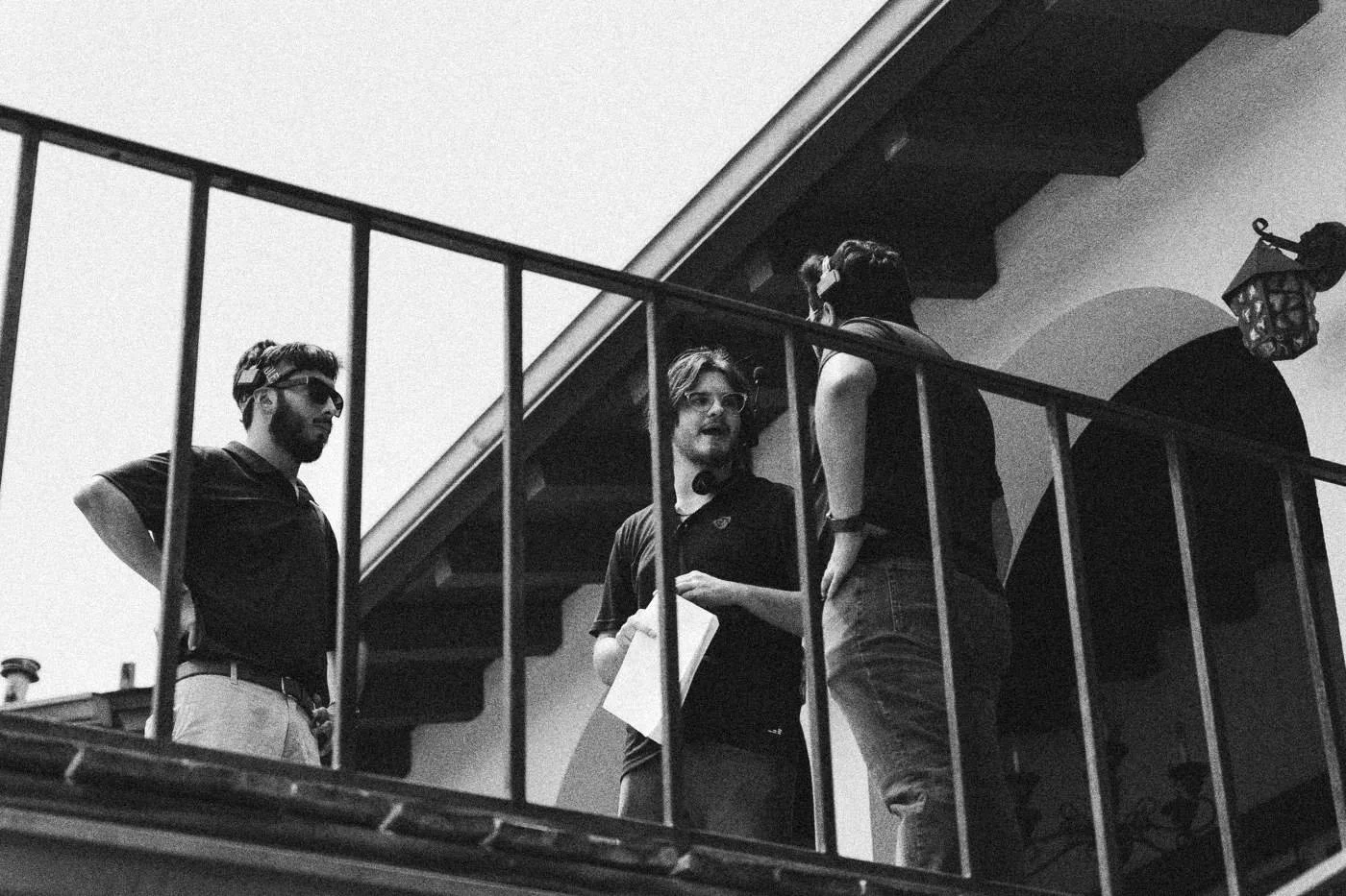 Behind the scenes on INERTIA: crew members stand on a staircase balcony against a bright sky.