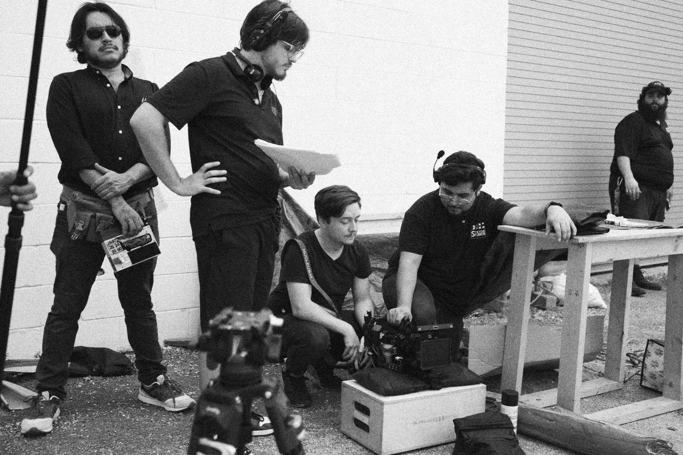 Behind the scenes on INERTIA: crew members wait by a white wall while one crouches at a camera.