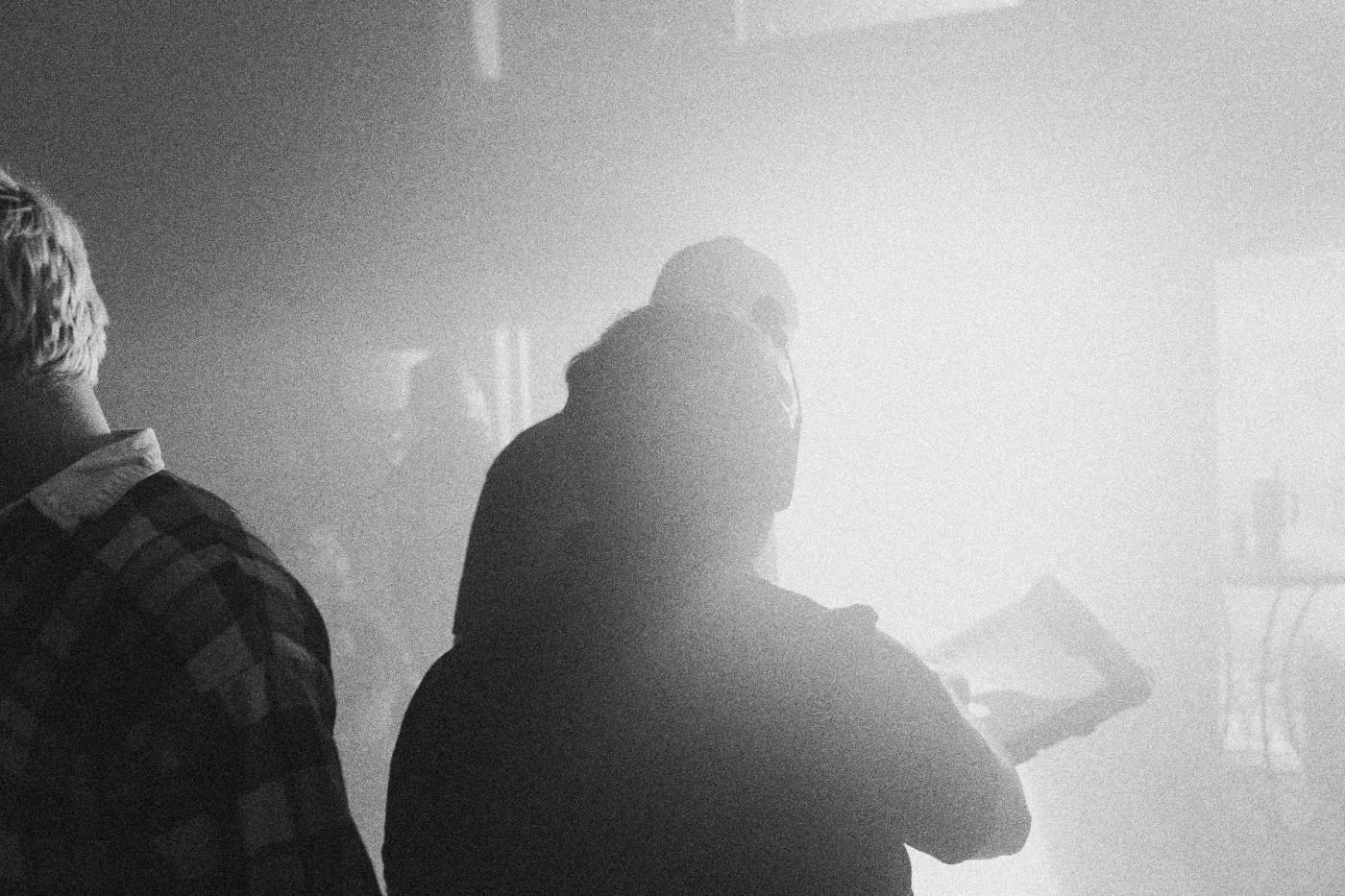 Behind the scenes on INERTIA: a crew member holding a tablet stands in silhouette against a bright light in haze.