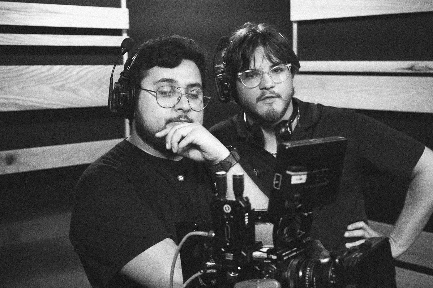 Behind the scenes on INERTIA: two crew members in headsets watch the camera's monitor in a recording studio, one with a hand at his chin.