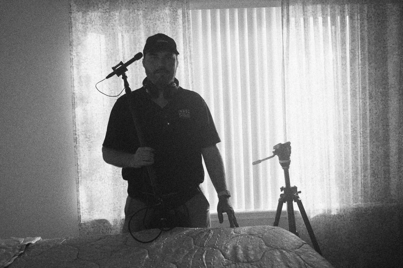 Behind the scenes on INERTIA: a boom operator stands in silhouette against window blinds in cool light.