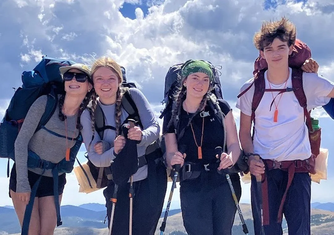 Students with backpacks smiling at the top of a hike