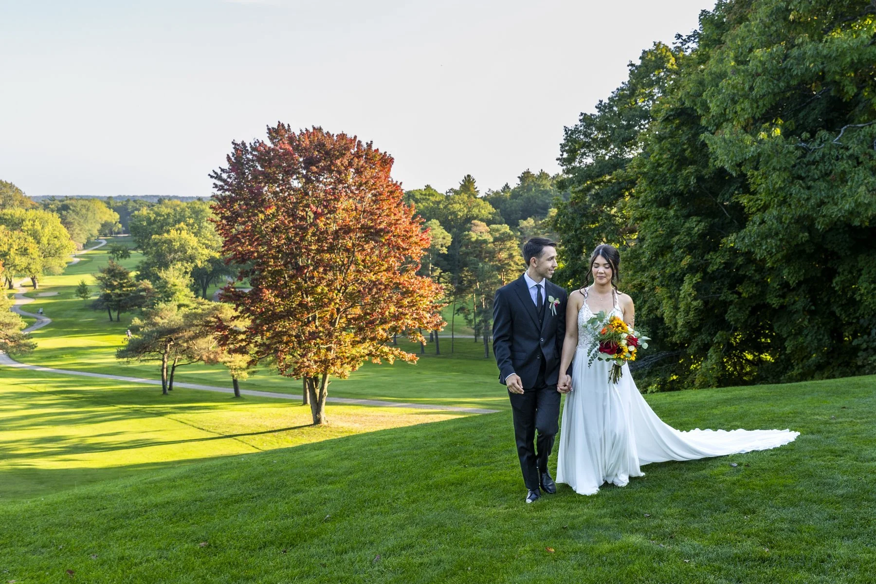 Couple walking across a golf course lawn beside an autumn tree