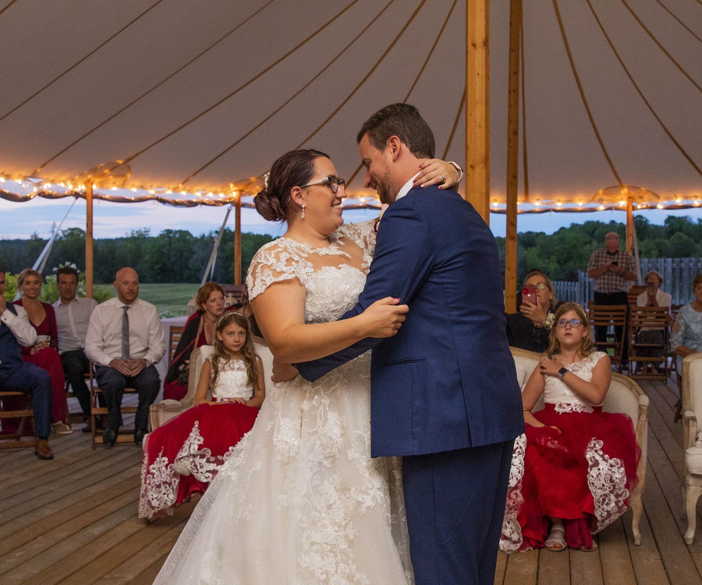 Bride and groom smiling at each other during their first dance under string lights