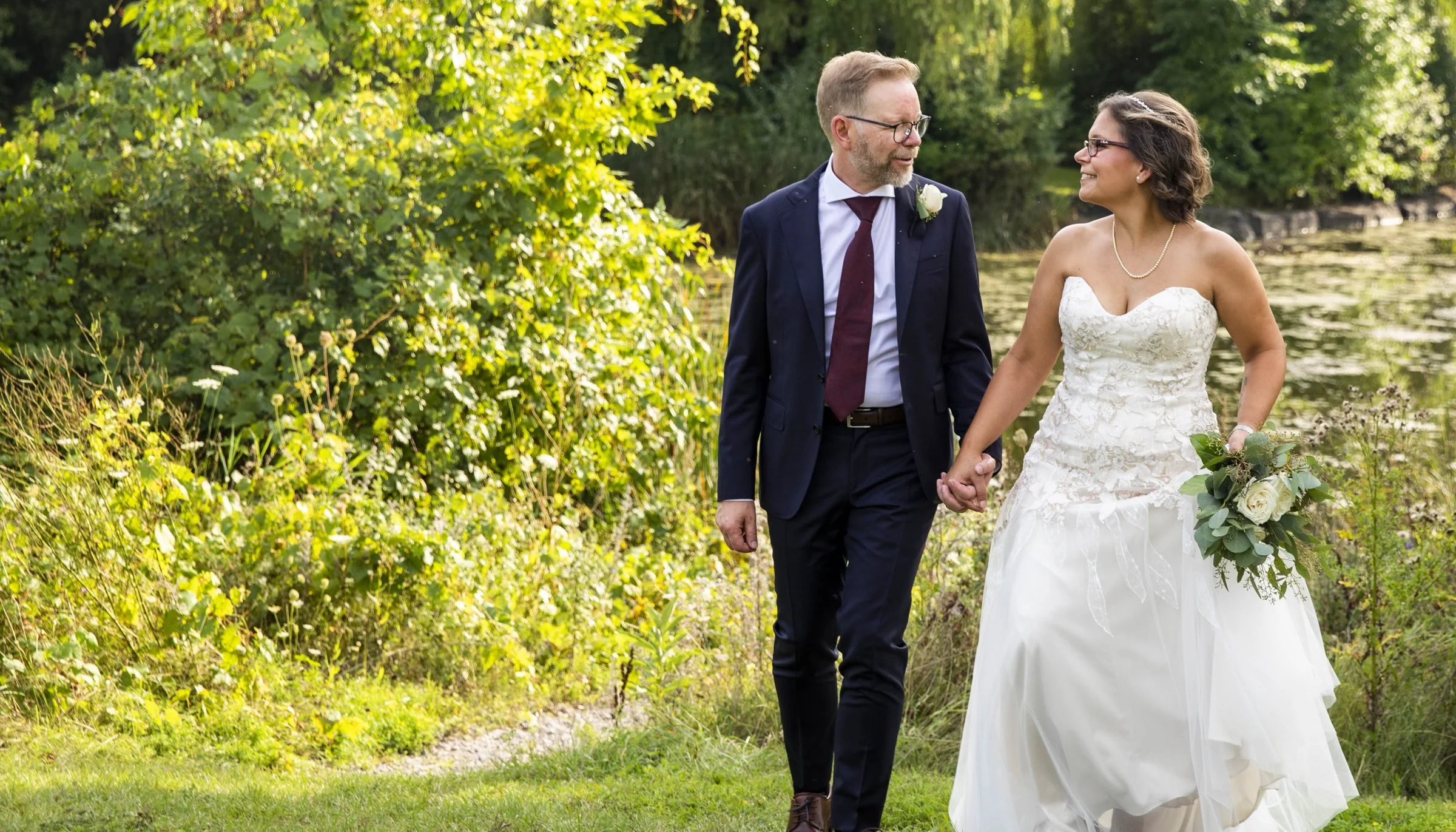 Couple walking hand in hand beside willow trees and a pond