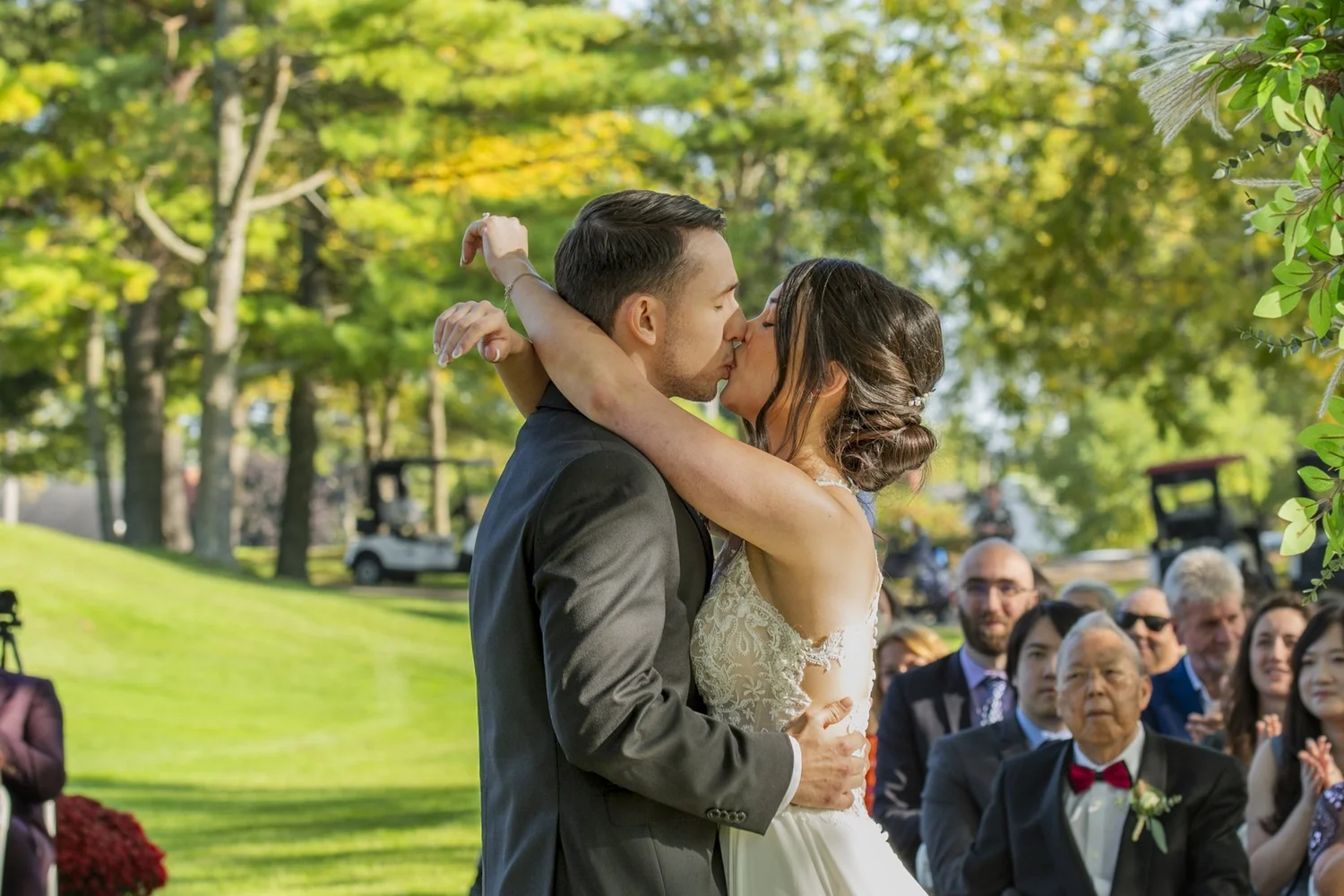 Bride throwing her arm around the groom for their first kiss as guests cheer