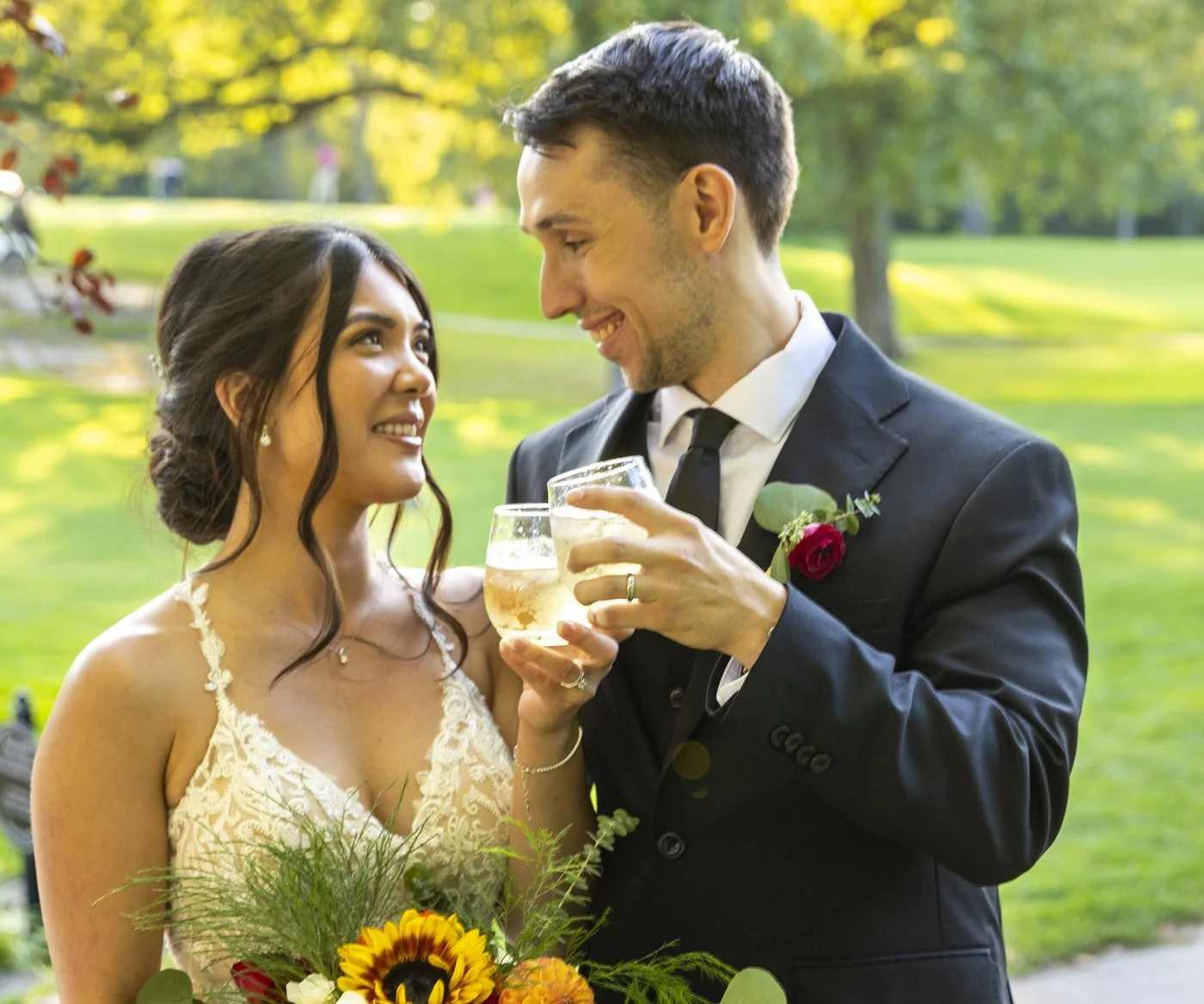 Bride and groom smiling as they toast each other outdoors