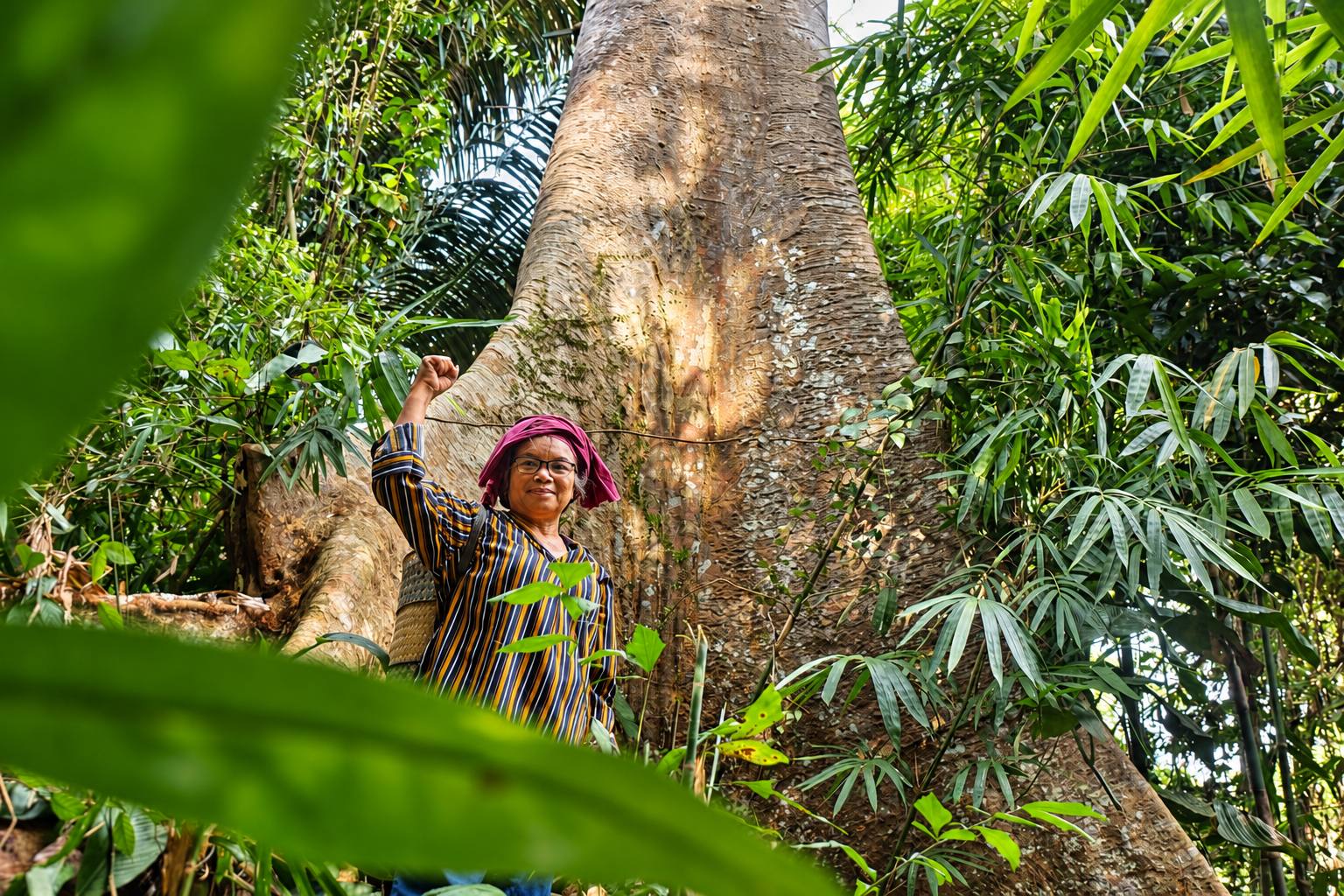 Dayak person standing proudly beside a large hardwood trunk