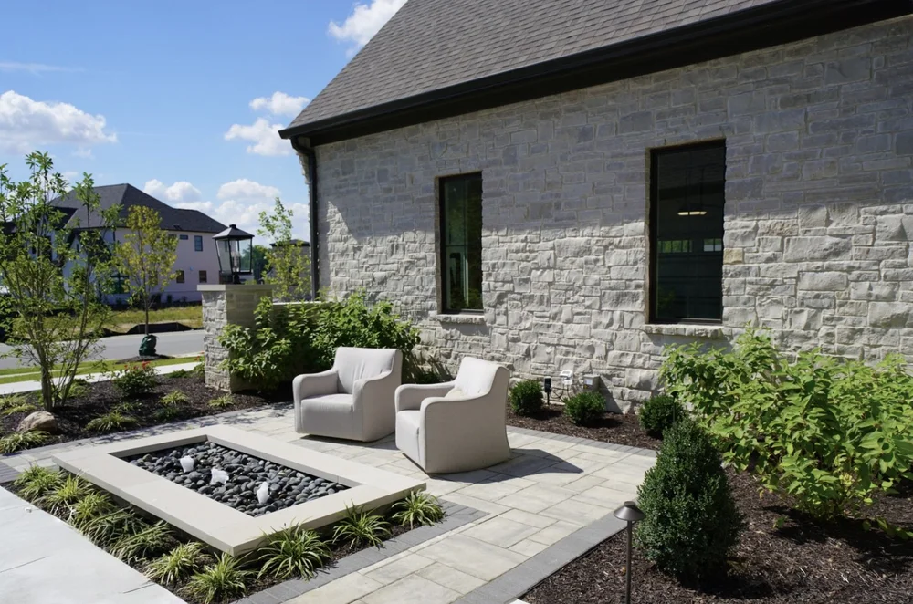 Byron ashlar veneer wraps a gabled elevation above a paver terrace with a square fire pit and lounge seating.