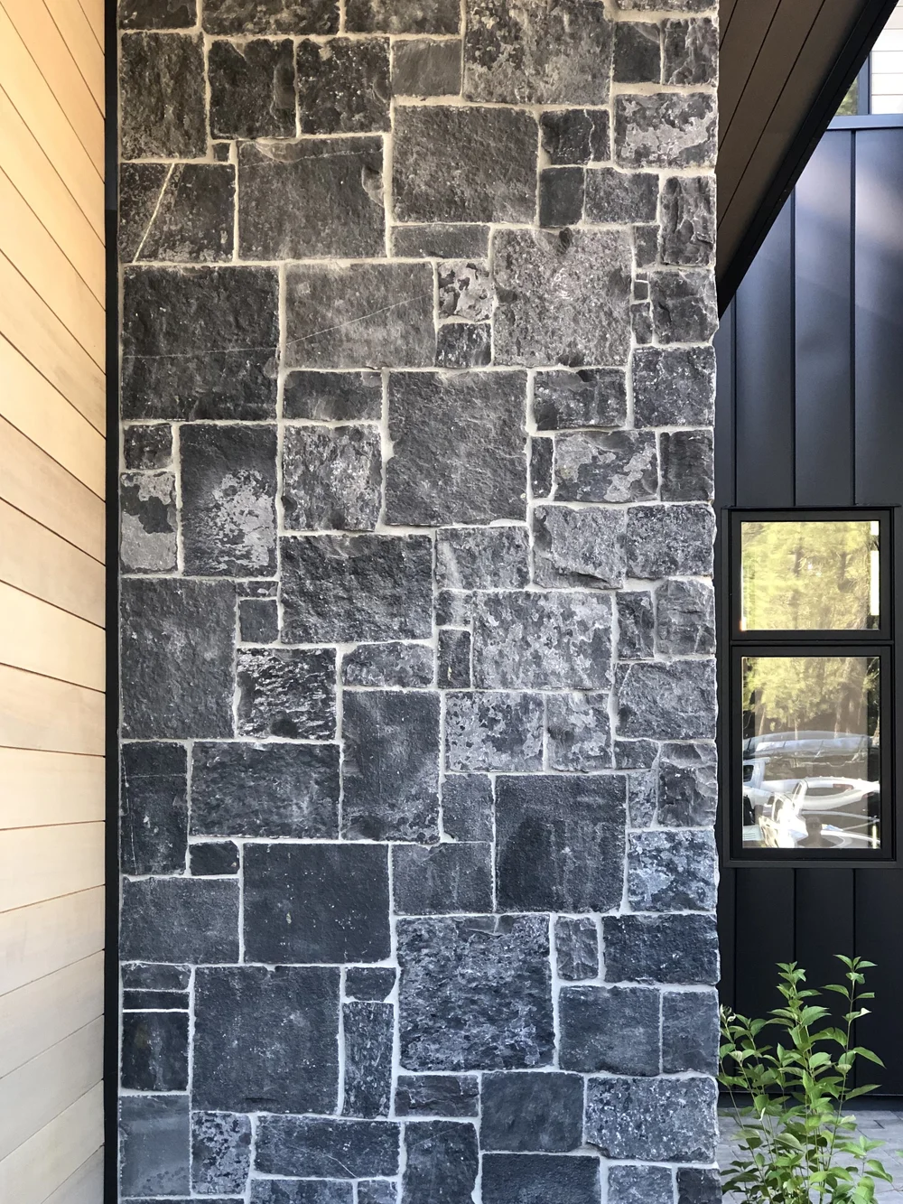 A tall run of Black Pearl meets wood siding on one side and black panel on the other, its pale joints reading bright against near black stone.