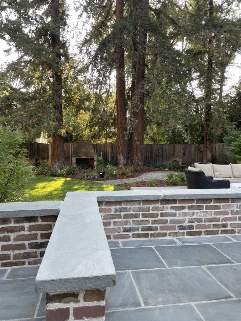 A thick Bluestone cap tops the brick seat wall, running out over the patio toward the fireplace beyond.
