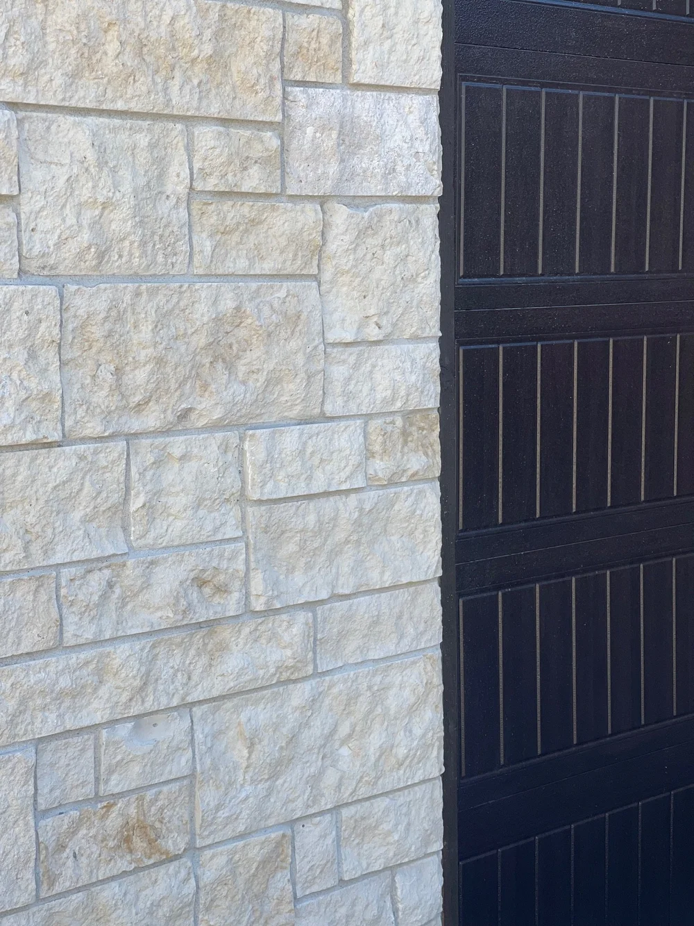 Close view of Cream split-face ashlar veneer beside a dark paneled garage door.