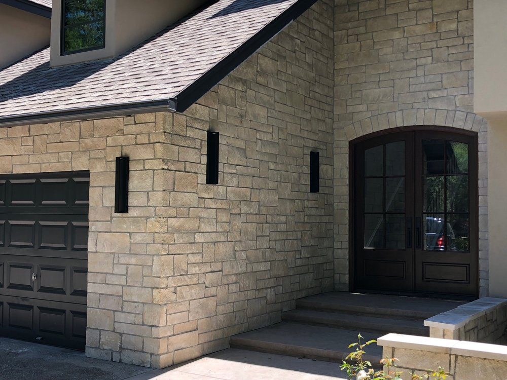 Buff ashlar veneer in split and natural faces with flush grout joints across an entry and garage facade.