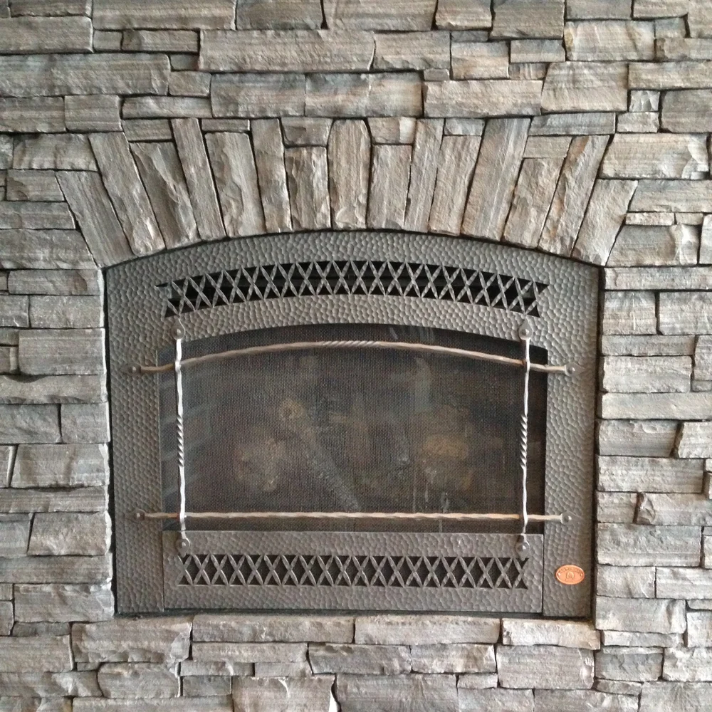 Black Rundle Stone in fine ledge courses surrounds a hammered bronze firebox door, the coursing stepping over its arch.