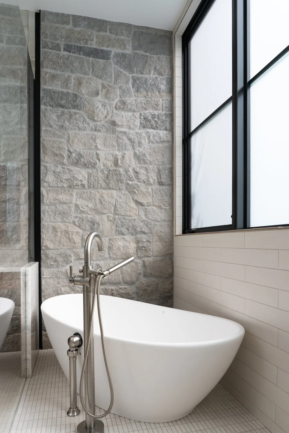 Gray Variegated fills a bathroom wall beside a freestanding tub and a black framed window.