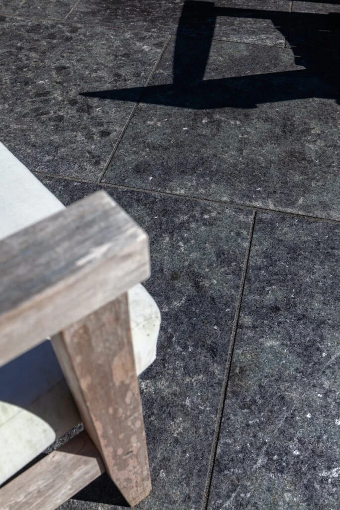 Flamed Saint Henry Black pavers seen close, tight sawn joints between large-format slabs with a weathered wood chair leg at the edge.