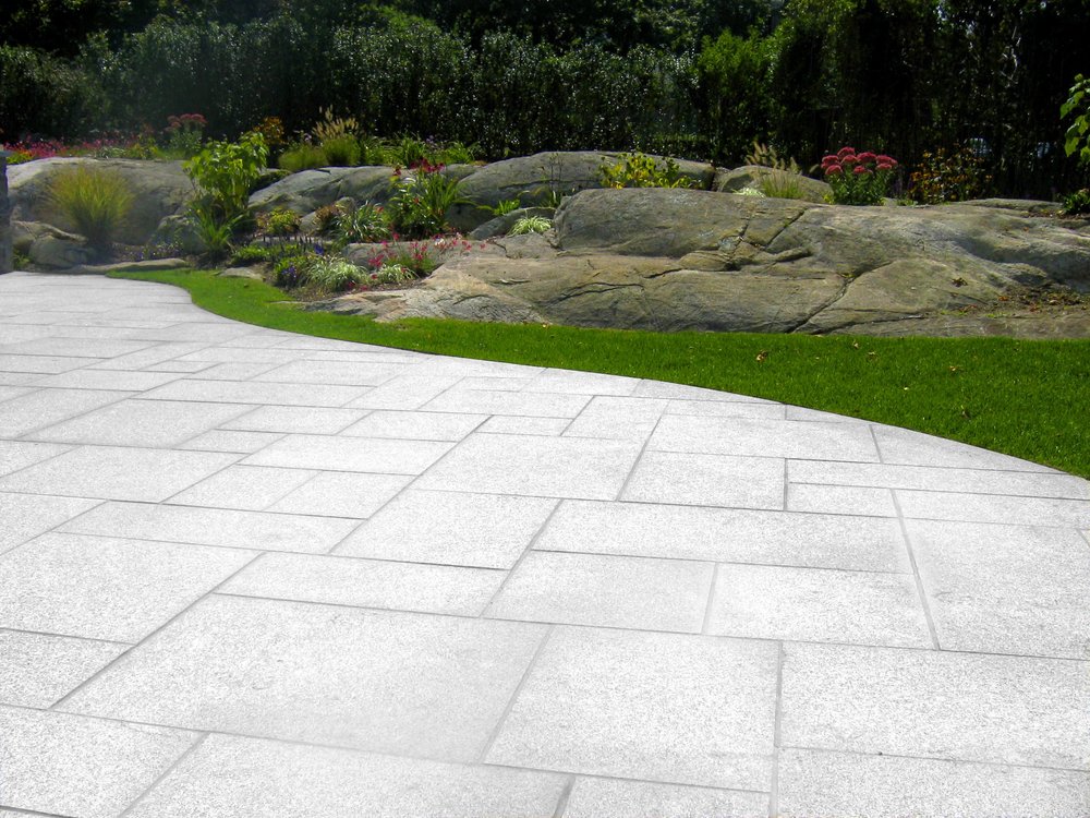 A flamed Woodbury Gray terrace curves past lawn to a run of glacial boulders.