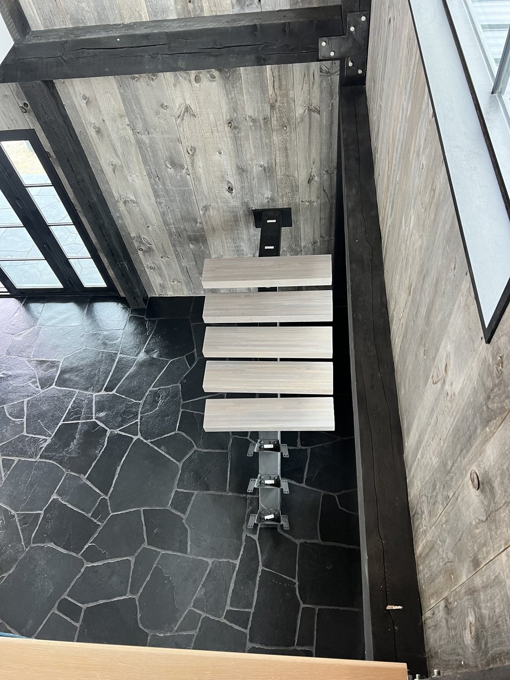 Black Slate irregular paving spreads below a run of floating treads, seen from the landing above.