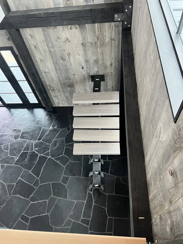 Black Slate irregular paving spreads below a run of floating treads, seen from the landing above.