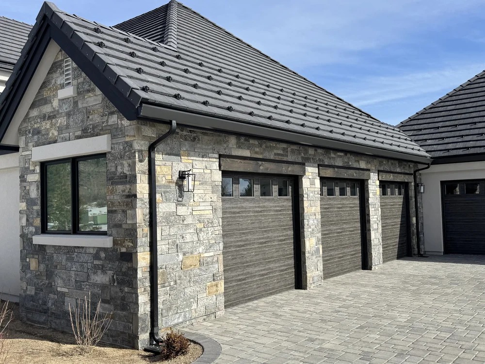 Graphite ashlar wraps a gable end and the piers between three garage bays under a tile roof.