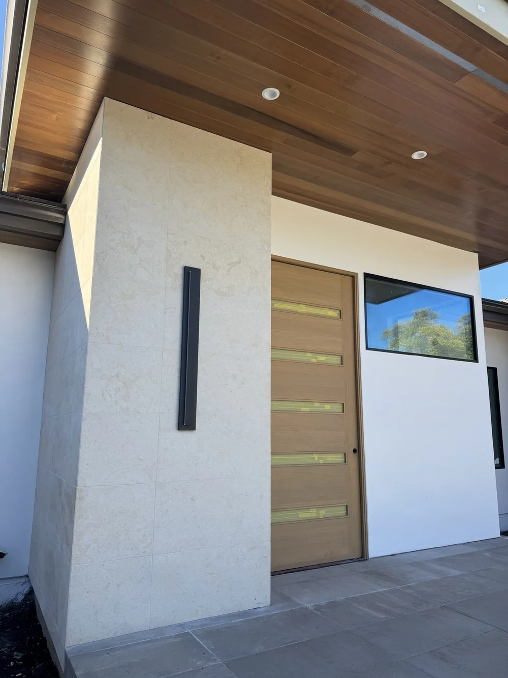 Brushed Cream panel veneer cladding an entry pier beneath a wood soffit, beside the front door.
