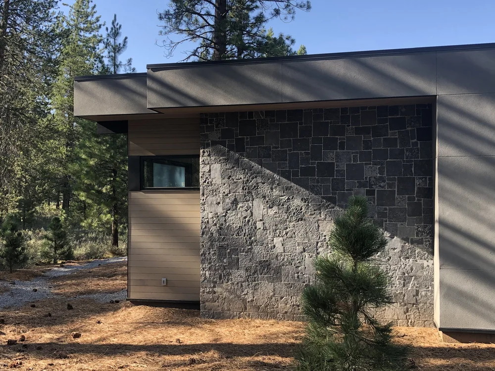 Black Pearl turns the corner of a low modern elevation among the pines, wood siding running back to a recessed entry.