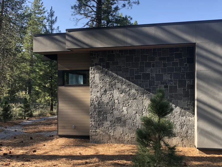 Black Pearl turns the corner of a low modern elevation among the pines, wood siding running back to a recessed entry.