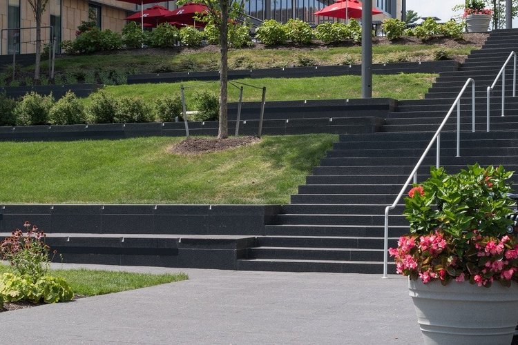 Cambrian Black steps and seat edges terrace a planted campus slope above the plaza paving.