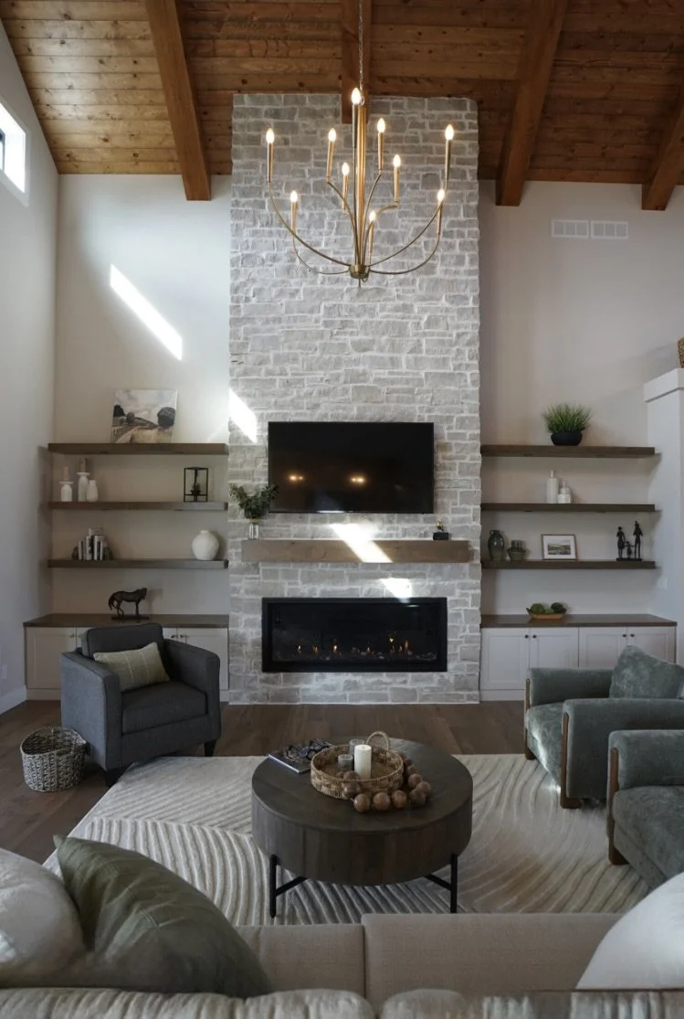 Byron ashlar veneer climbs a chimney breast to a beamed vaulted ceiling above a linear firebox, flanked by floating wood shelves.