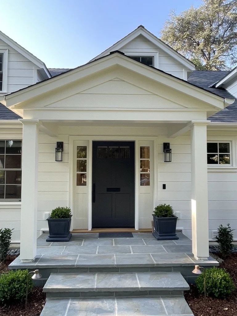 Bluestone steps and landing climb to a black front door between paired lanterns and planters.