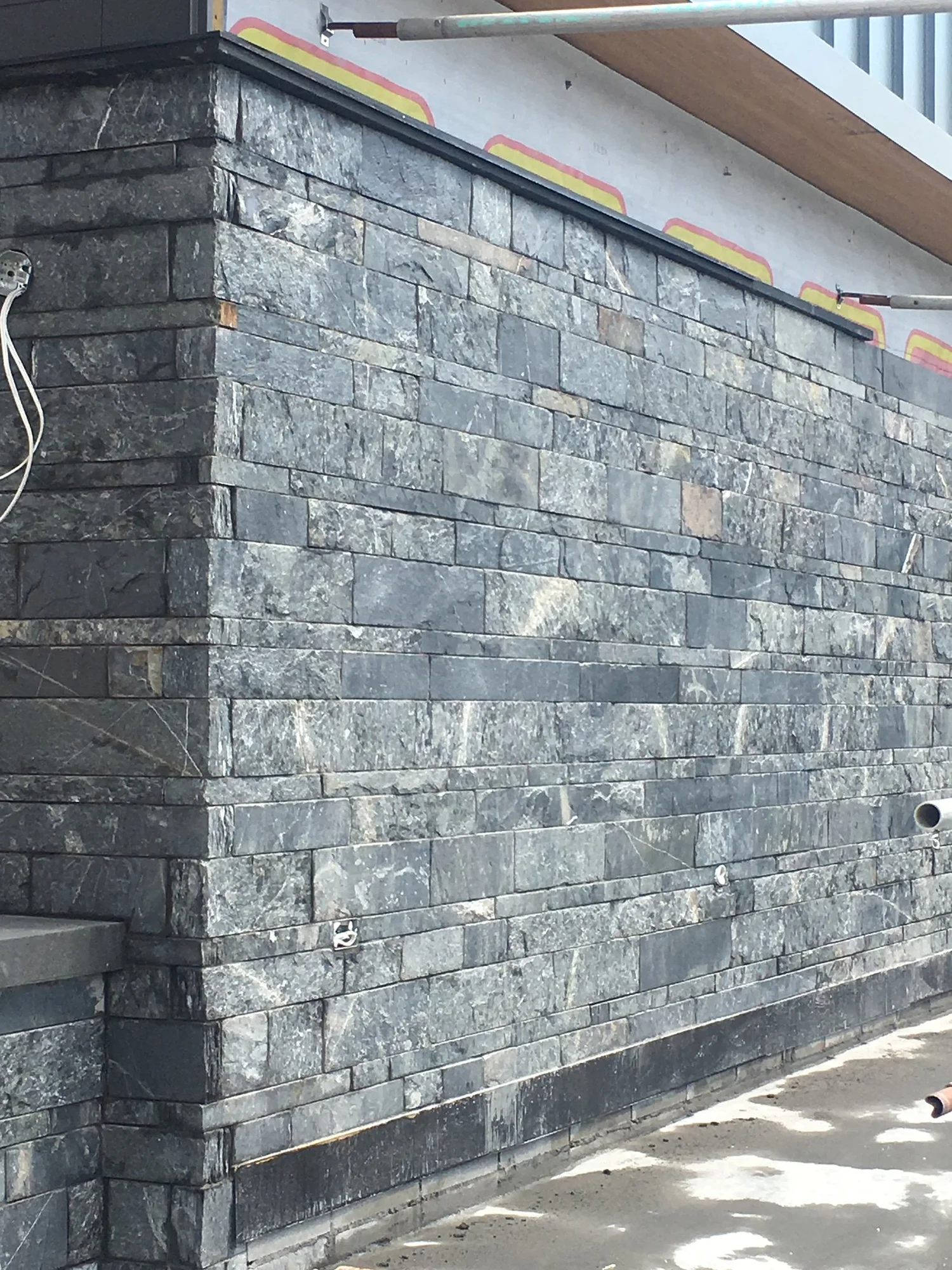 Black Rundle Stone in full veneer runs a long low wall under a painted eave, its courses varied in depth and colour.