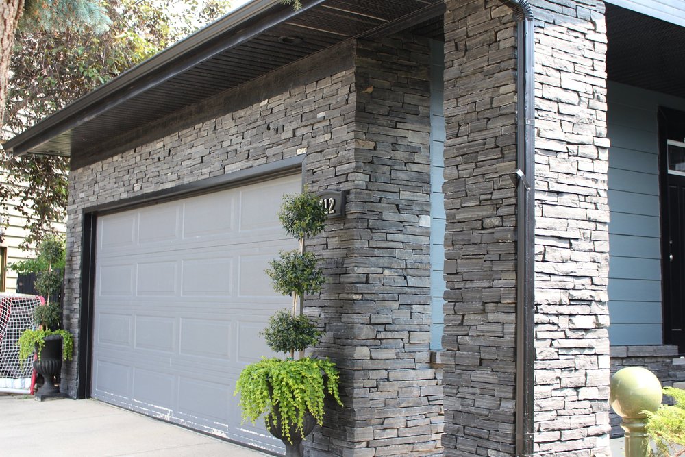 Black Rundle Stone stacks in tight ledge courses around a garage bay and up the corner piers of a flat roofed house.