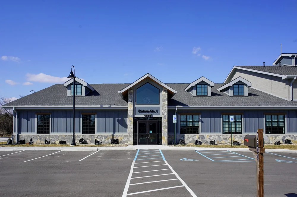Graphite mosaic picks out the entry gable of a low commercial building above its parking court.