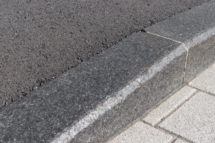 Cambrian Black curb stones run between asphalt and paver sidewalk, a chamfer easing the flamed top edge.