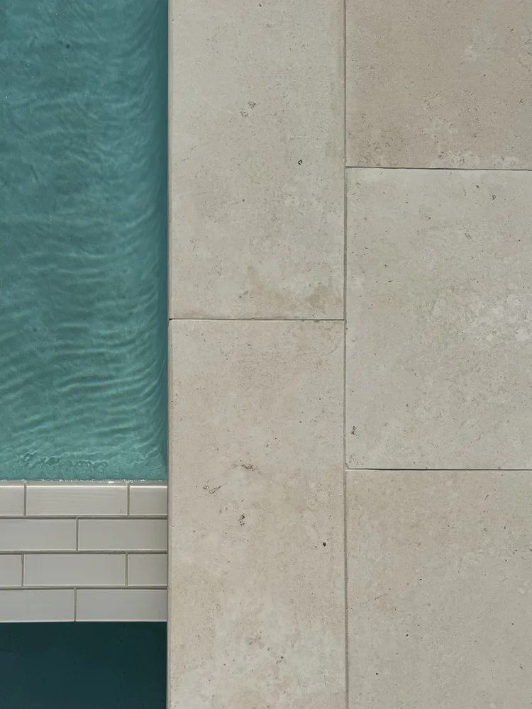 White bevel-edge pool coping over honed white pavers at the water's edge.