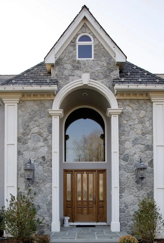 Bluewater flanks an arched entry surround, the stone running up into the gable above tall wood doors.