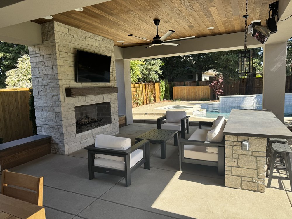 A Norway fireplace anchors a covered patio, the stone carrying across to the bar wall with the pool beyond.
