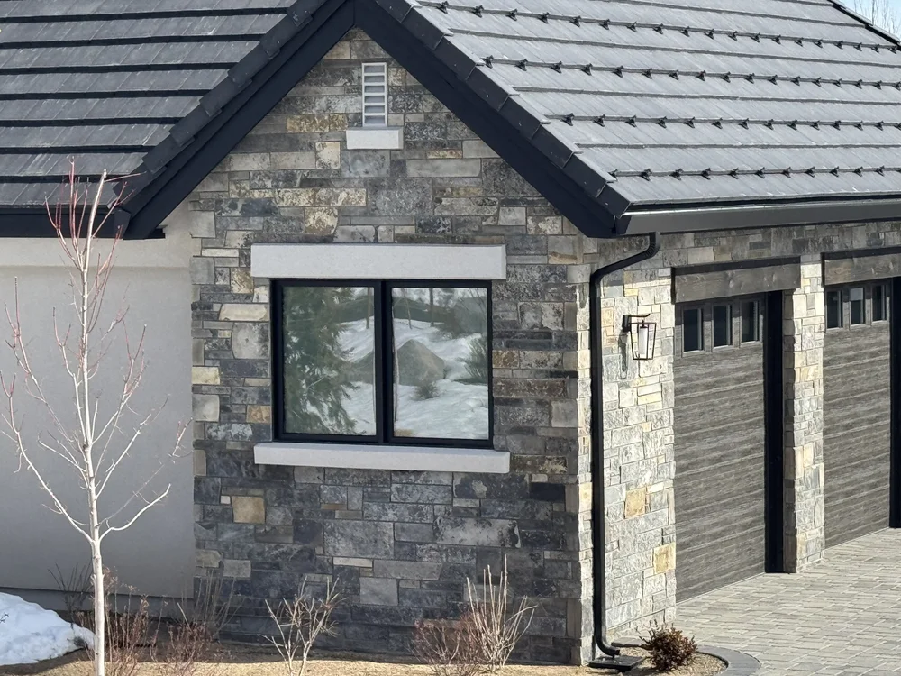 Graphite ashlar fills a gable around a black sash window, the garage piers carrying the same coursing.