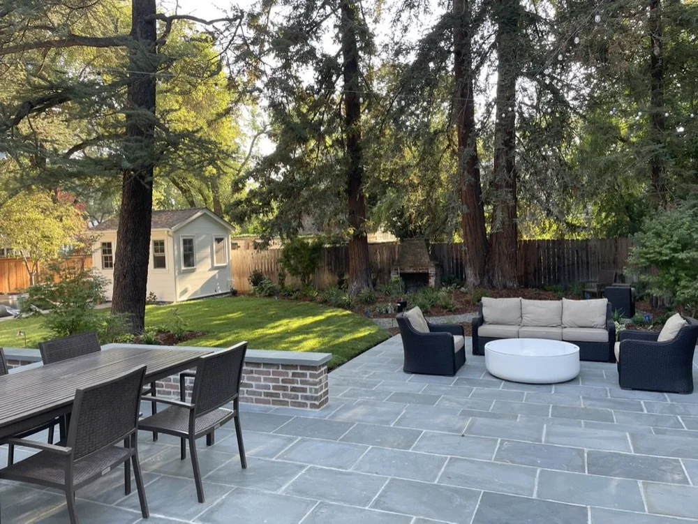 Bluestone spreads across the full patio between a dining set and a lounge group, the capped planter wall dividing them.