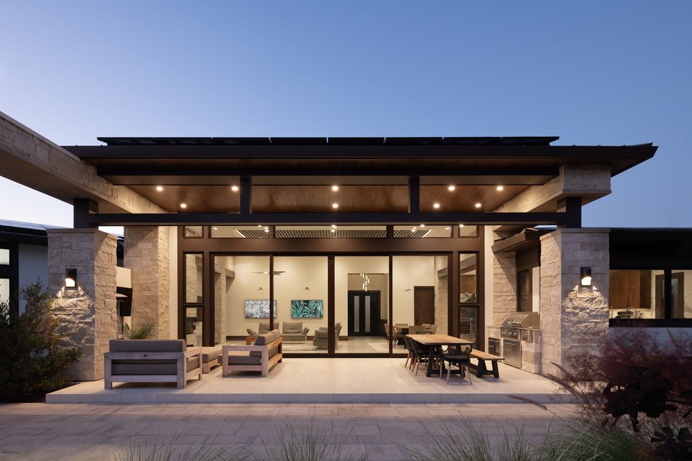 Buff coursed veneer in a split face with dry-stack joints across an outdoor kitchen and patio at dusk.