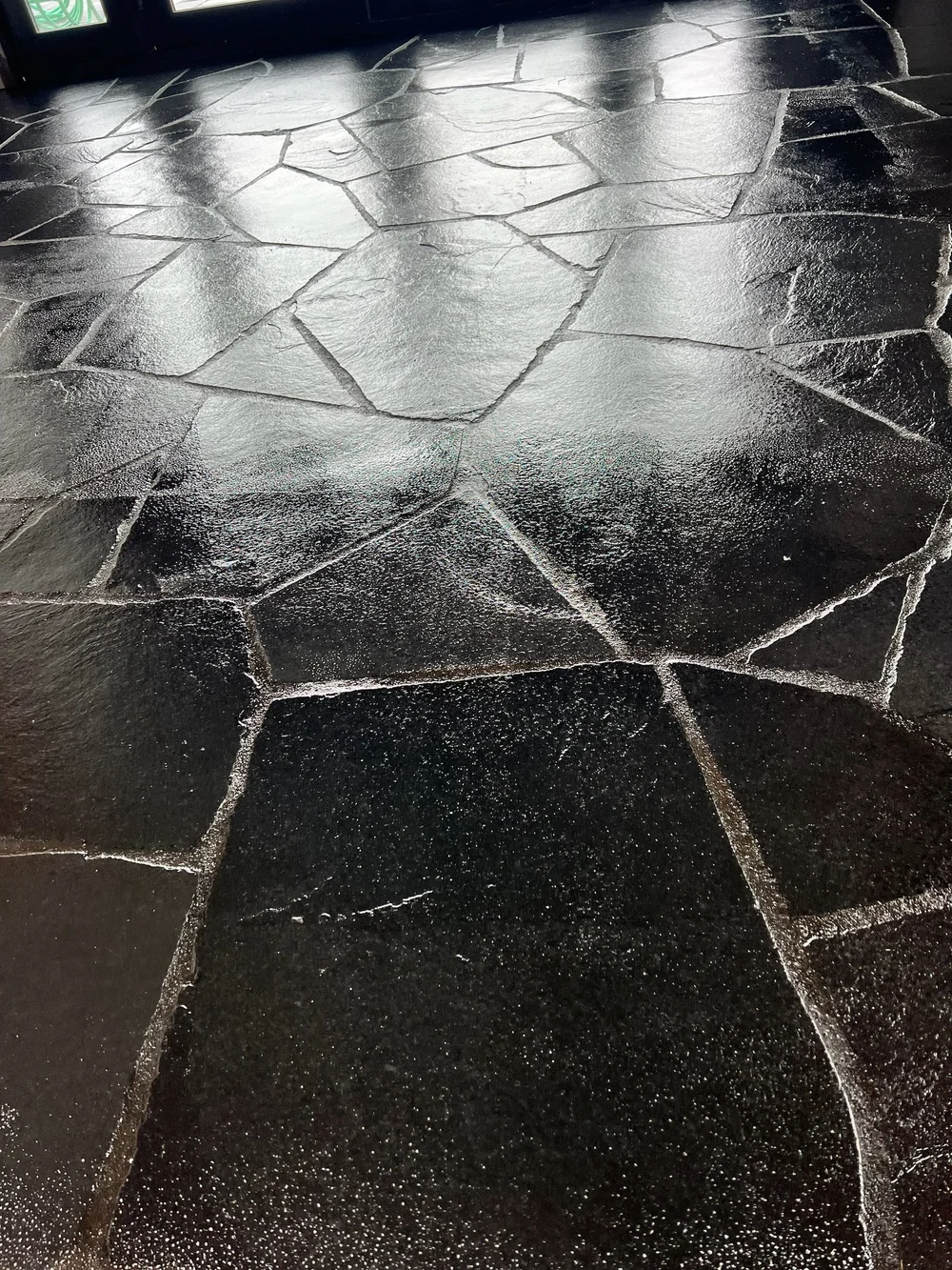 Black Slate irregular paving catches low sun across an interior floor, cleft faces reading almost black against pale joints.