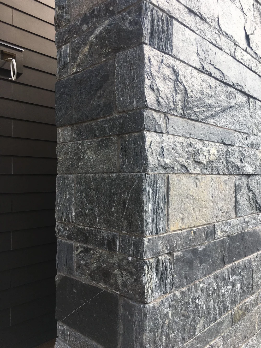 Black Rundle Stone in full veneer turns a corner in thick split courses, quartz veining catching the light against dark siding.