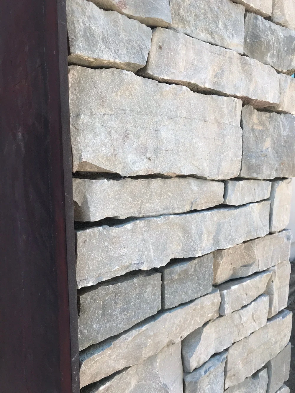 A dry-stacked Mayville ledge wall runs past a dark timber post in raking light.