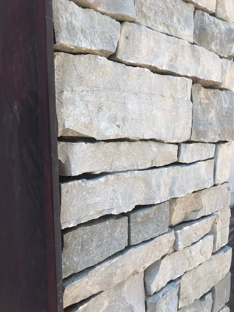 A dry-stacked Mayville ledge wall runs past a dark timber post in raking light.