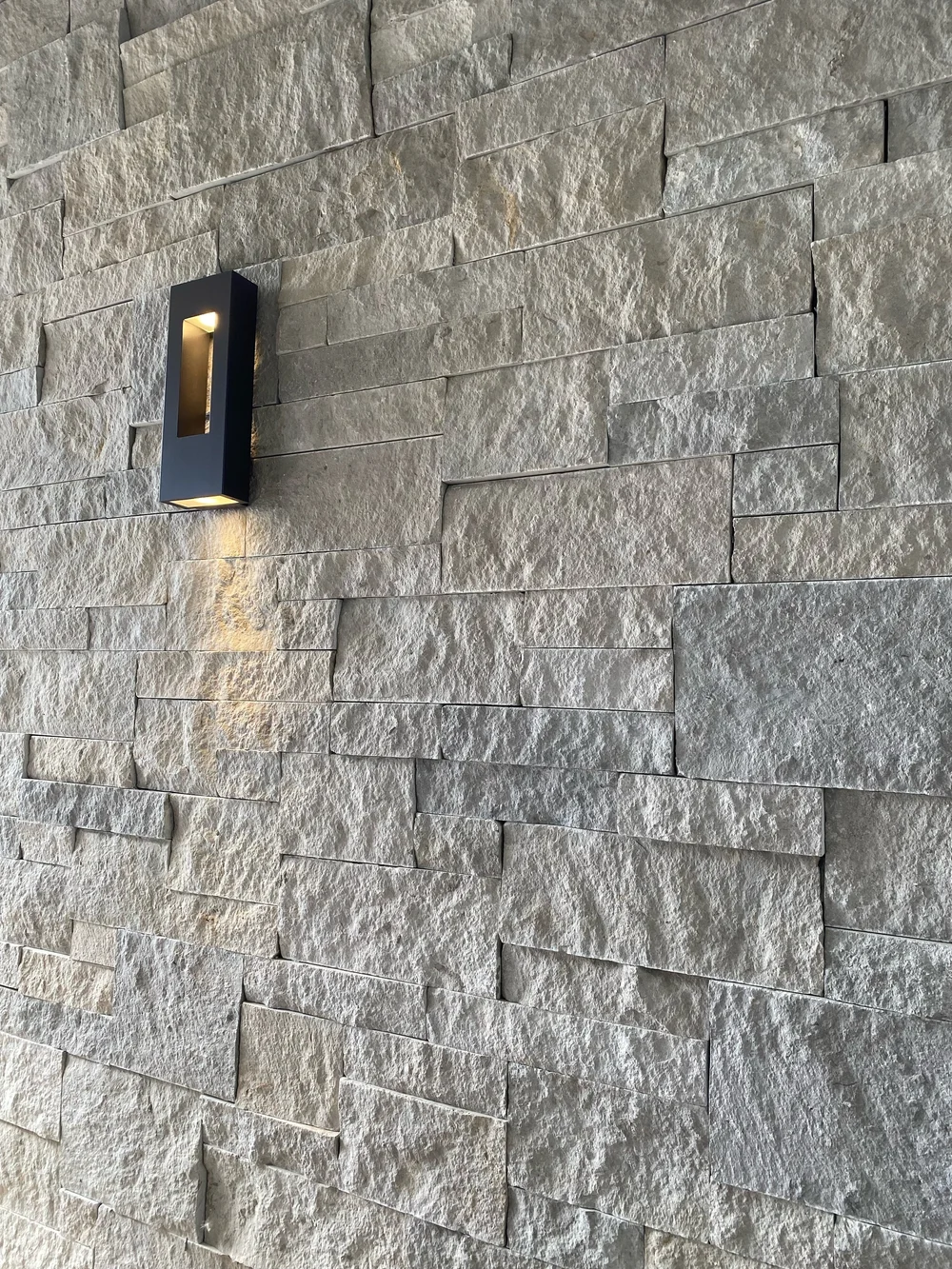 Gray Variegated in long low courses with sawn heights, a slim sconce washing the split faces.