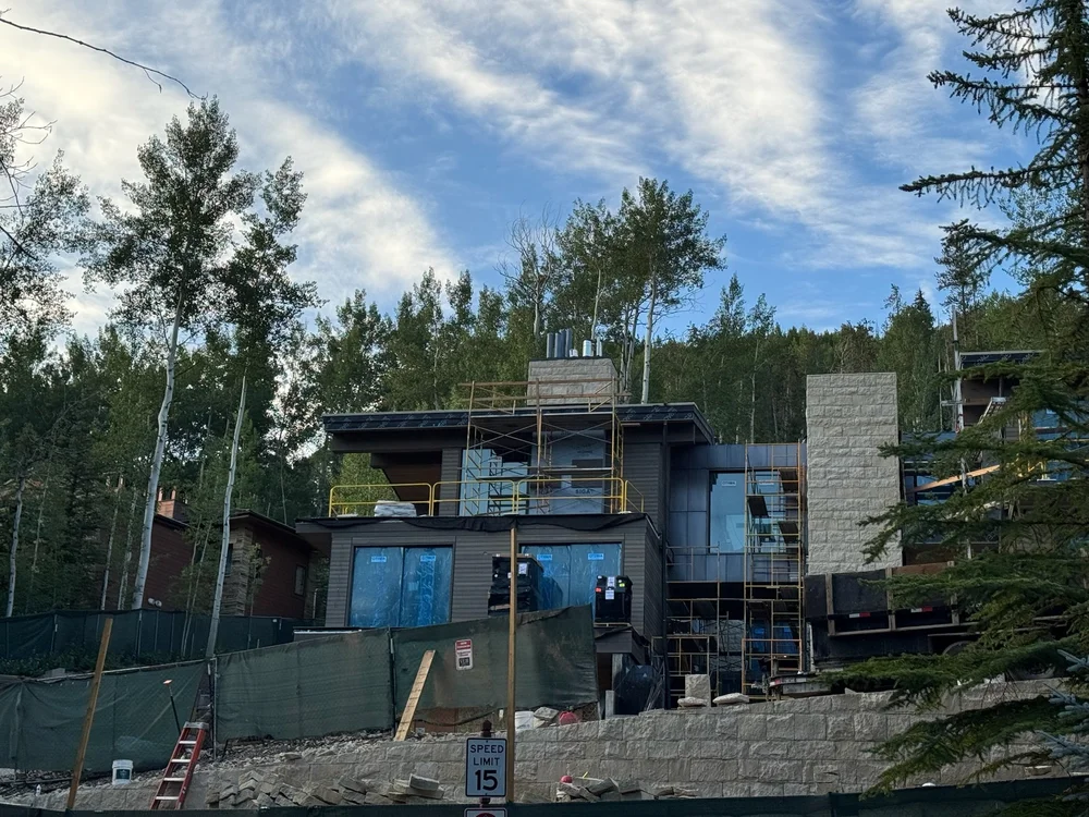 A mountain home under construction, its Buff coursed veneer chimney and stair tower rising against the aspens.