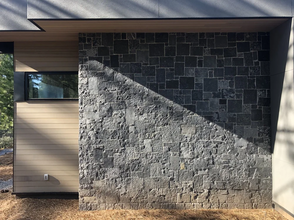 Black Pearl clads a full exterior bay beside horizontal wood siding, a low sun raking a diagonal across the split faces.